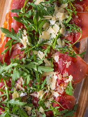 Pizza Parma. Pizza Prosciutto. Freshly baked Pizza Parma with a thin crispy crust, topped with prosciutto, arugula, and shaved Parmesan. Served on a rustic wooden board with a dark background