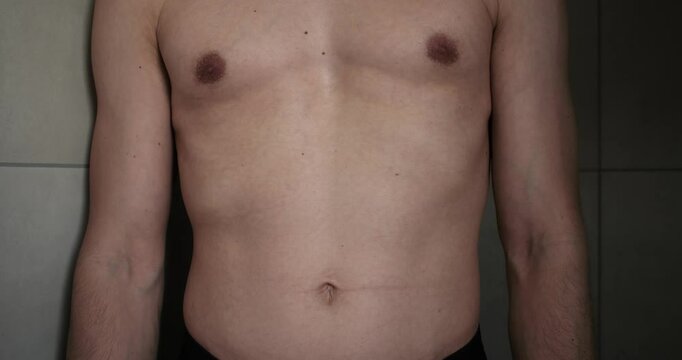 Medium shot of an average medium trained man in his late 30s. Checking physique in the mirror and doing different poses with the belly. Flexing muscles.