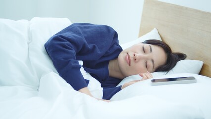 ベッドでスマートフォンを操作する女性