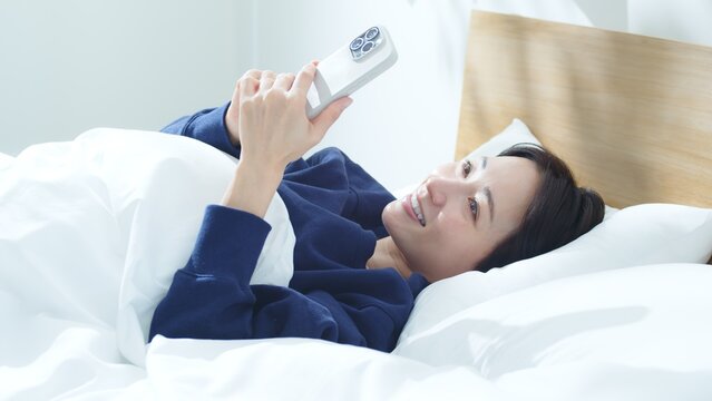 ベッドでスマートフォンを操作する女性