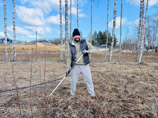 a man raking dry grass in spring at his country plot