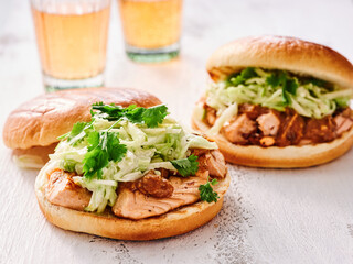 Juicy salmon burgers are beautifully garnished with crisp lettuce and cilantro, served alongside chilled beverages in a cozy dining atmosphere perfect for a flavorful meal