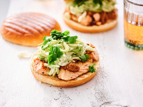 Juicy salmon burgers sit proudly on a rustic wooden surface, crowned with crisp greens and fresh herbs, alongside a refreshing drink, inviting a satisfying culinary experience