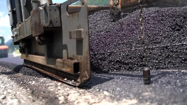 Asphalt paver screed during asphalt paving process, paving a new layer of asphalt at road construction site, close-up, low angle