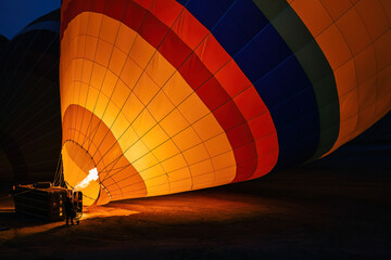 Close-up of a colorful hot air balloon being inflated with fire at night, highlighting vivid patterns and fabric texture. This image represents adventure tourism, travel preparation, and outdoor activ