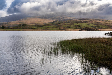 Calm water on mountain lake with moody clouds over distant mountain range