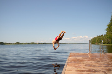 Man in swim trunks diving into water from a pier. Capturing a dynamic summer jump under the sun.