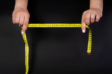 yellow tape measure in hands isolated on dark background