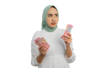 Pensive young Asian woman in green hijab and white blouse holding bunch of money and looking up with doubtful expression isolated on transparent background