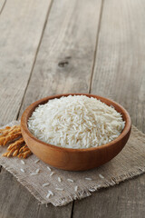 White rice fills wooden bowl standing on rustic table, accompanied by sprig of stalks