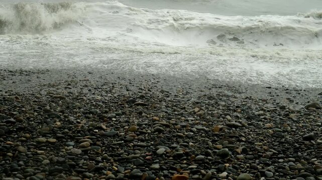 Stormy amazing crushing water waves in sea in overcast weather on pubble beach. Sea storm, power of water and weather, seascape on stone coast. Waves washing stones on coastline.