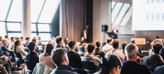 Female speaker giving a talk on corporate business conference. Unrecognizable people in audience at conference hall. Business and Entrepreneurship event