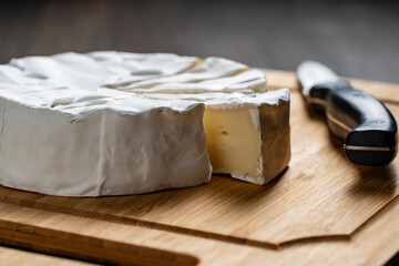 Cutting of white soft moldy Camembert cheese on a wooden cutting board with knife , closeup