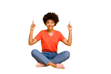 Full length body size photo of cute pretty sweet curly girl pointing up to show you sales sitting on floor with legs crossed wearing orange t-shirt jeans denim isolated vivid color background
