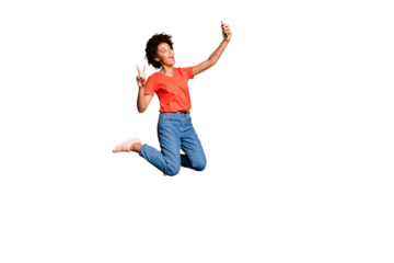 Full size photo of crazy beautiful funky curly hair girl blogger jump use smartphone take selfie make v-signs wear red t-shirt denim jeans sneakers isolated over yellow bright color background