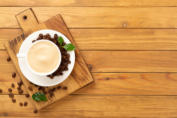 Cup of coffee with coffee beans and leaves on wooden background,top view