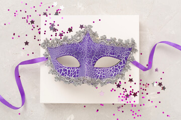 Bright carnival mask with confetti on concrete background, top view