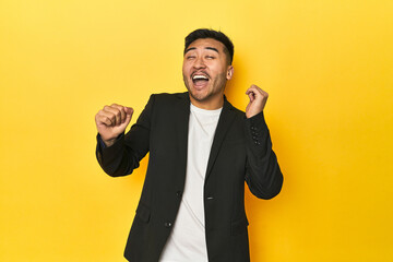 Asian man in black business jacket on yellow studio dancing and having fun.