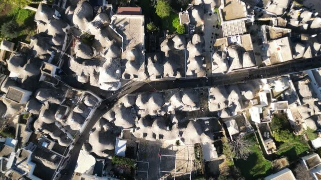 Aerial View of Alberobello's Trulli: High-angle shot showcasing the charming trulli houses of Alberobello, with their unique cone-shaped roofs, forming a picturesque townscape under the sun. 