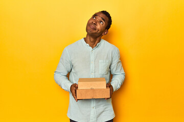 African American man with food boxes, yellow studio, dreaming of achieving goals and purposes