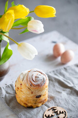 Easter Bread or Kulich with raisins. Easter yeast twisted cake Cruffin, painted eggs and tulip flowers on a stone background. Easter food.