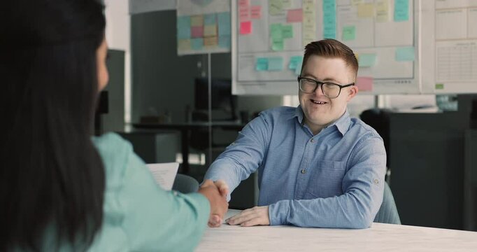 Positive down syndrome business professional man getting job in inclusive company, giving handshake over table to recruit manager after interview meeting, smiling