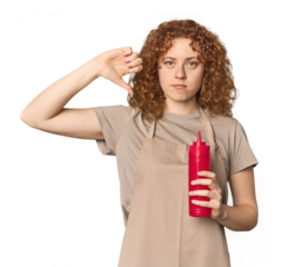 Young Caucasian redhead woman with ketchup showing a dislike gesture, thumbs down. Disagreement concept.