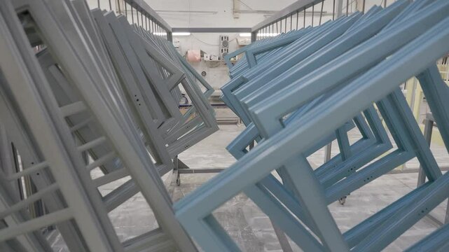 Multiple blue and gray window frames are suspended on hooks in a clean, organized workshop environment, drying after industrial spray or powder coating process