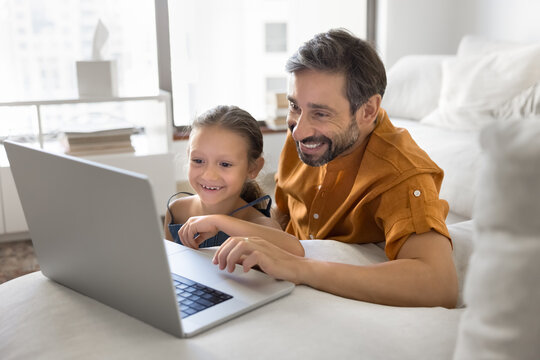 Parental guidance. Happy smiling family single foster father preteen adopted daughter spend weekend at living room explore online gaming surf internet on notebook for learning in calm joyful manner