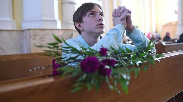 An 12 year old boy attends Mass on Palm Sunday. a child prays in a Catholic church, in front of him is a bouquet of willow, flowers and a palm leaf.