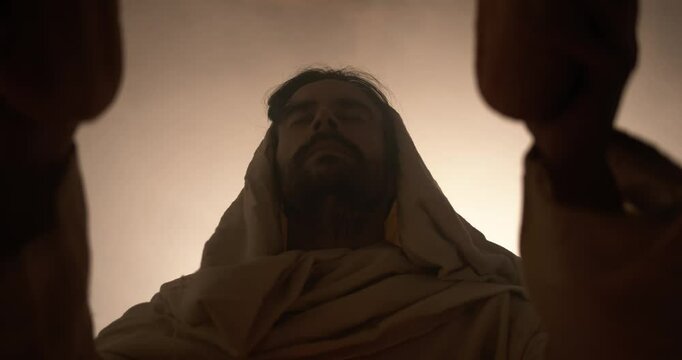 Jesus Christ in white hooded robe holding bread as he stands in glowing, bright light praying. Perfect for representation of Jesus as the bread of life, last supper, communion, Christian sacraments.
