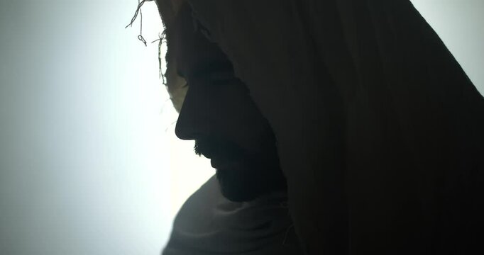 The face of the resurrected Jesus Christ standing inside the tomb in bright, dramatic, glowing, holy light as representation of the Easter Sunday resurrection in cinematic slow motion.
