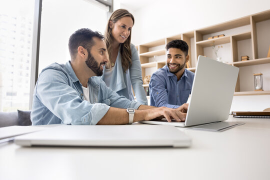Productive teamwork. Mature businesswoman and two younger male colleagues of different ethnicities collaborate to solve problem using notebook discuss project on screen analyze data in corporate app