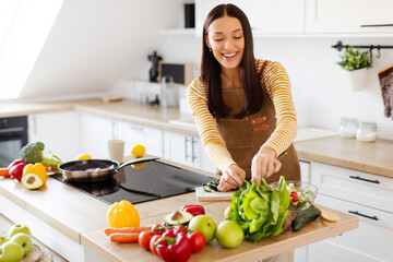 Beautiful housewife making dinner, taking lettuce leaves while cooking salad, standing in kitchen. Home made dinner preparation concept