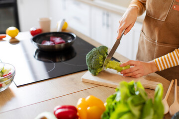 Woman cutting broccoli on chopping board, preparing healthy meal in the kitchen, cooking meat and vegetables, closeup cropped shot