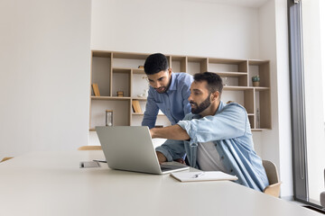 Teaching apprentice. Experienced millennial male office worker software developer project manager training mentoring younger colleague gen z student intern share skills explain work on notebook screen