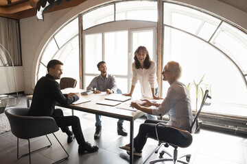 Happy lady leader CEO manager laughing with business colleagues at project presentation at office meeting. International professional startup boss speaking to diverse board team. Company people work