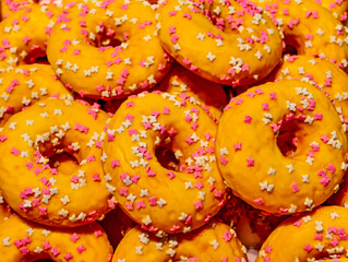 Close-up of yellow glazed donuts decorated with tiny pink and white butterfly-shaped sprinkles. A bright and cheerful dessert ideal for spring or summer-themed food, parties, kids' events and bakery.