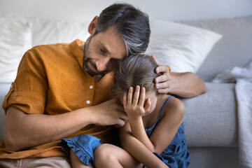 Grieving suffering dad hug upset depressed tween daughter crying on floor at home offer support...