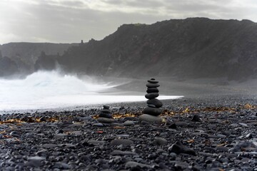 Black rock mountain stands still on a volcanic beach with dark sand and cold atmosphere