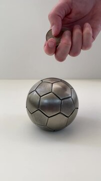 Coins being inserted into football shaped money box (piggy bank). The coins are Norwegian kroner coins.