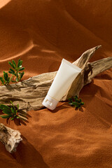 Unlabeled tube placed on a barren tree. On the trunk, there are tiny desert shrub growing from the sand and cracks of the trunk. Brown sand with fine sand grains. Vertical photo with desert concept.