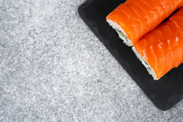 Fresh salmon sushi rolls served on a black slate plate in dim lighting