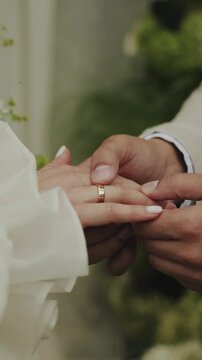 Hands close-up, bride and groom holding hands and exchanging wedding rings during a wedding ceremony near the arch. Vertical shot. 