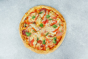 Freshly baked pizza with cheese, pepperoni, and vegetables on a gray surface