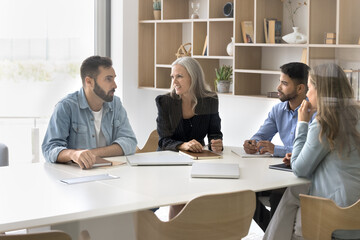 Business team of four diverse professionals of different age ethnicity discuss project create...