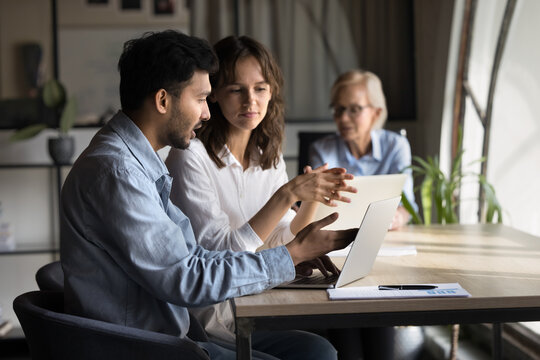 Indian mentor businessman gives explanation to digital finance project, two focused diverse corporate businesspeople collaborate in front of computer laptop, look at screen, managing ecommerce sales