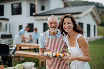 Older father and adult daughter preparing food for a family barbecue.