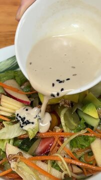 Fresh salad with vegetables, dressing pouring over for vibrant taste