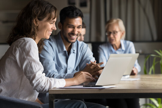 Two happy professional executives partners work with laptop, businessman and businesswoman use computer software, discuss online digital project, have fun effective collaboration in corporate meeting